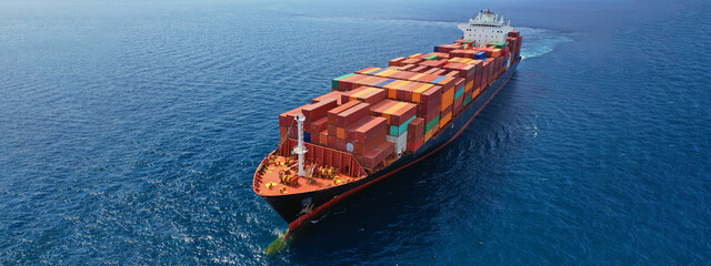 Aerial drone ultra wide photo of huge container ship cruising deep blue open ocean sea near logistics container terminal port