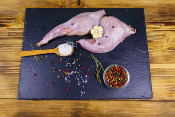 Wall Mural - Raw rabbit legs with spices on a black slate cutting board on wooden table. Top view