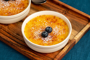 Wall Mural - Creme brulee in ramekin on wooden tray on dark linen tablecloth. Close up french vanilla cream dessert. Burned cream. Spanish crema catalana with caramelized sugar.