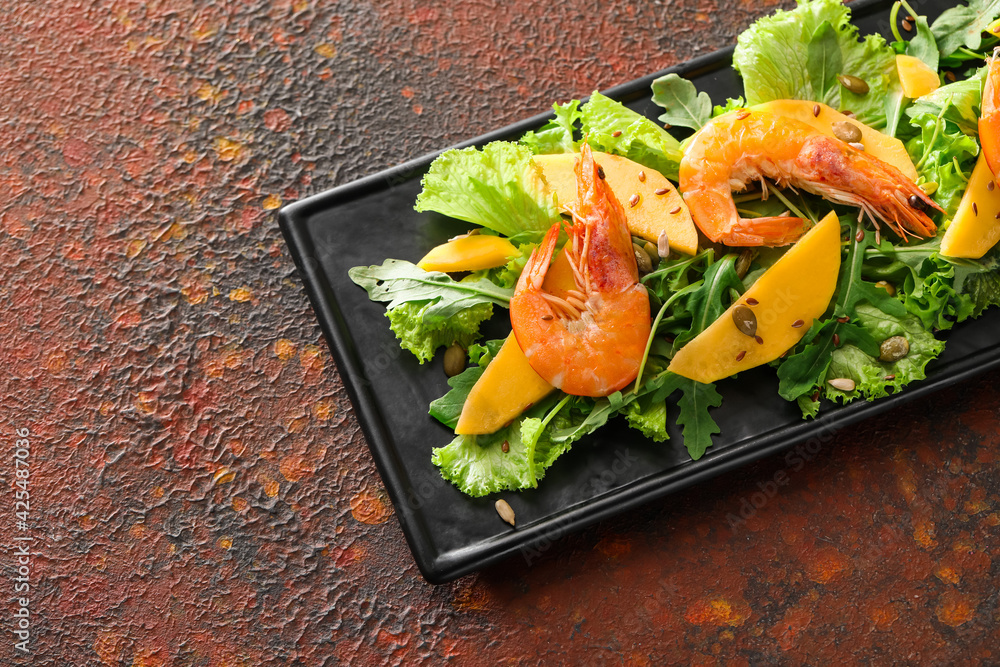 Plate of fresh mango salad with shrimps on grunge background