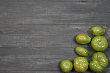 A group of green tomatoes is lying on a wooden table. Copy space.The concept of harvesting