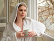 
Young, beautiful woman in a white robe with a cup of coffee stands on the balcony 