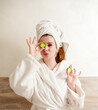 Young, beautiful housewife in a bathrobe playfully makes a cosmetic mask from cucumbers 