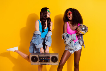 Photo of two young girl happy positive smile listen music boombox have fun disco ball african isolated over yellow color background