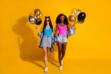 Sticker - Full length photo of brunette girlfriends walk hold balloons wear singlet denim jacket isolated on yellow color background