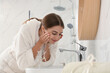 © New Africa - Young woman washing her face with water in bathroom
