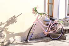 Street Decor, City Beautification, Pink Vintage Retro Bike Decorated With Flowers Stands By The Wall Of The House On A Sunny Day With Beautiful Shadows On The Facade Of The Building