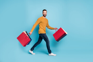 Canvas Print - Full size profile side photo of young happy positive cheerful man go walk with shopping bags isolated on blue color background