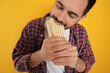 Young man eating tasty shawarma on yellow background, closeup