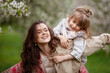 © fadzeyeva - Mother with child girl playing in blooming spring garden. Woman with daughter huging and having fun outdoors. Concept of happy family