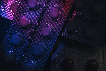 Fototapete - Pills or drugs in a package under neon light on a dark background pattern for design..