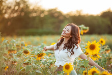 Young Asian Woman With Curly Hair In A Field Of Sunflowers At Sunset. Portrait Of A Young Beautiful Asian Woman In The Sun.