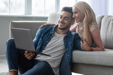 Wall Mural - Loving young arab man and woman using laptop at home