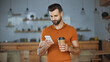 © LIGHTFIELD STUDIOS - bearded man using smartphone and holding coffee to go in cafe