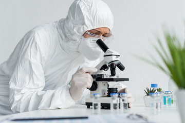 Wall Mural - Scientist in hazmat suit working with microscope near vaccines on blurred foreground