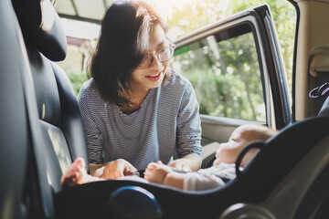 Wall Mural - Happy Smiling Asian Mother helping her little baby boy son to fasten belt on his car seat in the car for safety in transportation