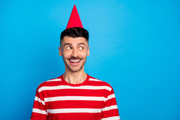 Sticker - Photo of dreamy cheerful young man wear birthday cone hat look empty space isolated on pastel blue color background