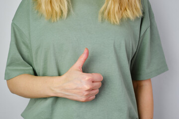 Wall Mural - Blond hair woman posing near a light wall. Beautiful young caucasian girl. Hand gestures. Emotion. Casual clothing. Studio model in work. Strong woman, future is female. Jeans and green blank t-shirt