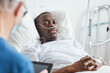 © Seventyfour - Portrait of African-American man lying in hospital bed and looking at doctor, copy space