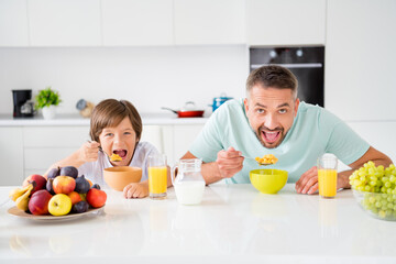 Canvas Print - Photo portrait of dad and son eating cereal with milk fruits having breakfast on white kitchen