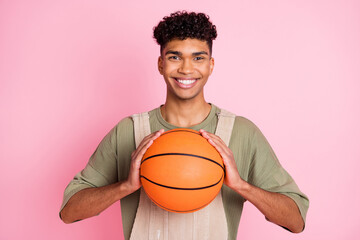 Sticker - Photo portrait of curly guy keeping ball on training smiling in stylish clothes isolated on pastel pink color background