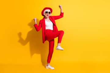 Full length body size photo of elder woman in red suit sunglass gesturing like winner isolated on bright yellow color background