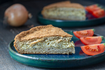 Slice of homemade onion quiche a baked cream and egg pie topped with cheese and green herbs