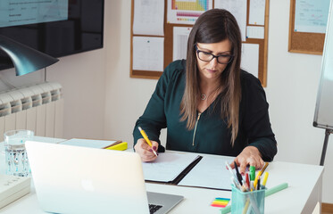 Wall Mural - Female professor holding online class for e-learning students and writing down notes.
Teacher working at home, video conferencing using laptop computer,  teaching online lesson for Math students