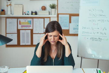 Female professor having headache while working at home. Teacher holding online class for e-learning students, sitting in her home office during class break and holding head with hands