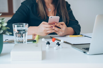 Wall Mural - Cropped photo of unrecognizable female chemistry teacher sitting at desk and holding mobile phone. Young professor or student having break with online class and using smartphone to send text message