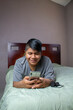 © cesar - Hispanic young man smiling making video call with cell phone lying in bed