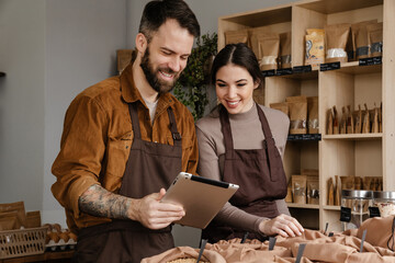 Smiling sellers man and woman using tablet while working in local shop