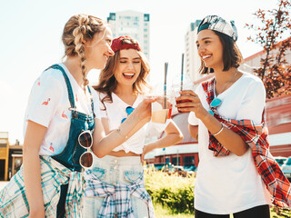 Wall Mural - Three young beautiful smiling hipster female in trendy summer clothes.Sexy carefree women posing outdoors.Positive models holding and drinking fresh cocktail smoothie drink in plastic cup with straw