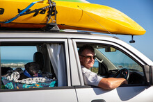 A Male Tourist Pauses To Take In The Seaside View. He Is Driving A Campervan With Kayaks On The Roof Rack And His Dog In The Back.