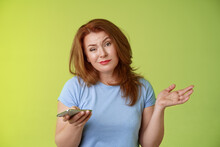 Well Meh. Indifferent Careless Hesitant Redhead Middle-aged Woman Mature Red Female Shrugging Hold Smartphone Smirk Bored Uninterested Hold Hand Aside Apathetic Attitude Green Background