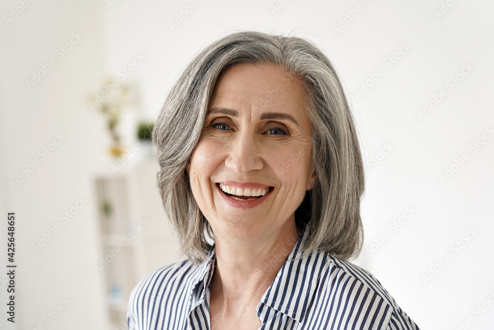 Cheerful satisfied 50s mature woman laughing looking at camera at home. Happy sophisticated classy mid age older gray-haired lady with white teeth dental smile posing for close up headshot portrait. - obrazy, fototapety, plakaty 