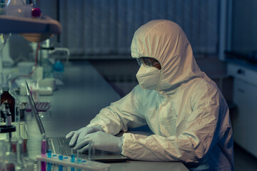 Sticker - Chemist in protective workwear and in mask sitting at the table and working online on laptop in danger chemical lab