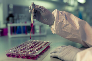 Sticker - Close-up of scientist in protective gloves holding pipette and taking purple liquid from test tubes at the table