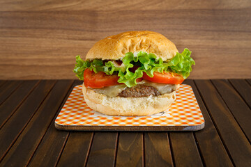 Delicious hamburger on wooden background. Burger with tomato, lettuce, meat and cheese.