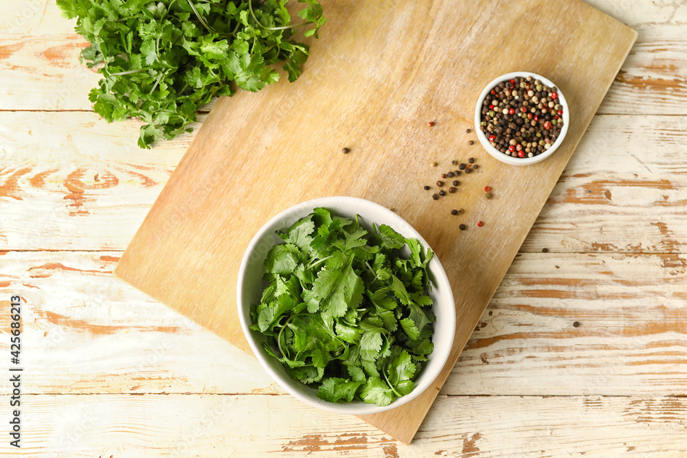 Bowls with fresh cilantro and peppercorns on light wooden background
