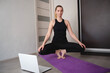 © Aleksandra Iarosh - young woman doing asana at home on yoga mat in front of laptop
