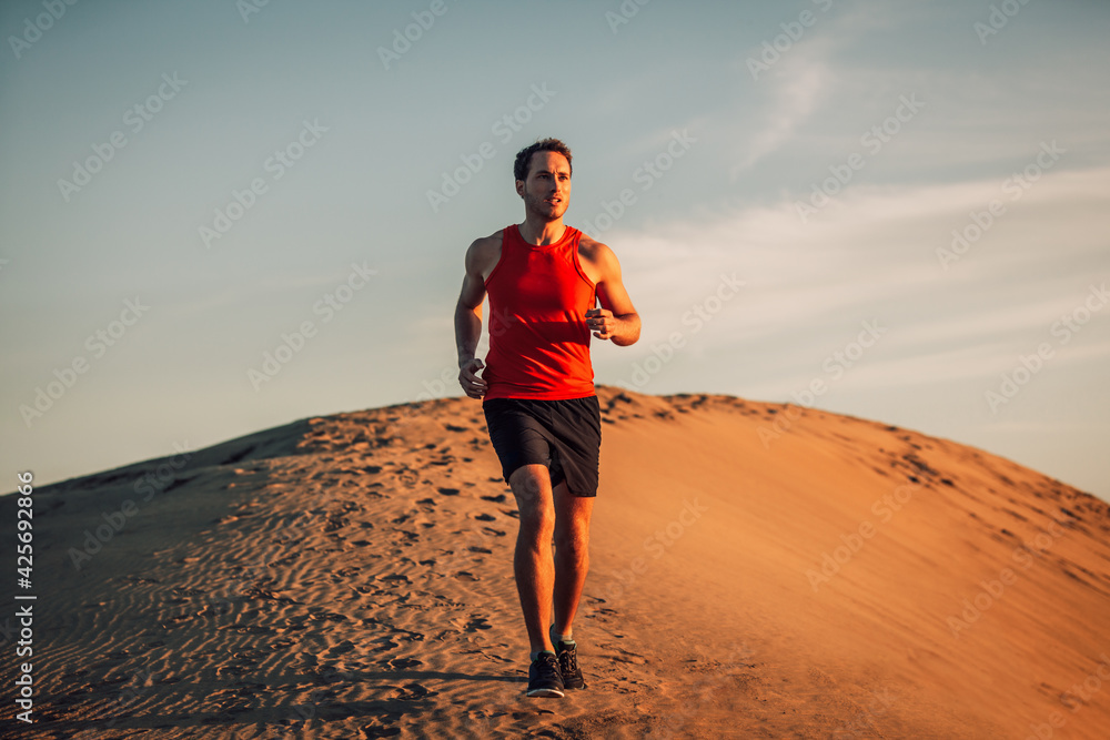 Trail runner athlete running man in desert sand dun in heat of summer sunset day. - obrazy, fototapety, plakaty 