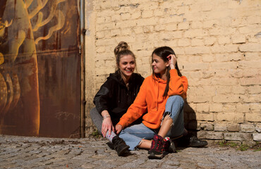 Two teenage skater girls are hanging out in the neighborhood, chatting and smiling at each other.