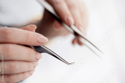 Obraz Dibond Close-up hand of master holds tools for eyebrow correction and eyelash extension tweezers and tongs on white background
