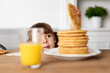 © Lisa Tichané - Young girl peeking behind kitchen table stealing a pancake