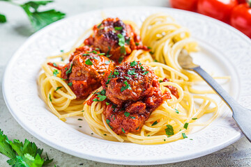 Canvas Print - Spaghetti pasta with meatballs in tomato sauce and herbs on white plate, close up. Comfort food concept.