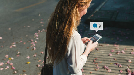 Canvas Print - Young woman using social media on her smartphone while walking the streets