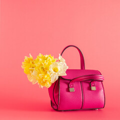 women small pink bag with fresh yellow narcissus on pink pastel summer background. minimal abstract art.