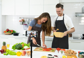 young caucasian couple who are blogger teaching people to cook healthy food via smartphone camera. family together concept