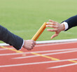 Businessmen pass on the baton in relay race in stadium